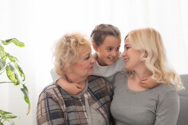 Three generations of women. Beautiful woman and teenage girl are kissing their granny while sitting on couch at home