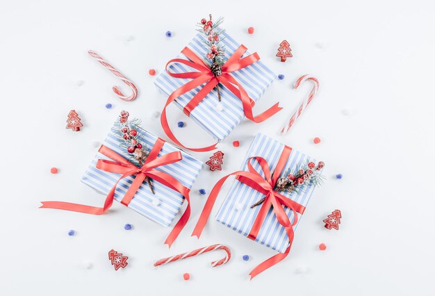 Three gift boxes in a blue strip with red ribbons sweets wooden Christmas trees and a fluffy ball of snow on a white