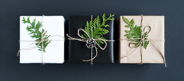 Photo three gift boxes with twigs of ceder and rope on dark background top view