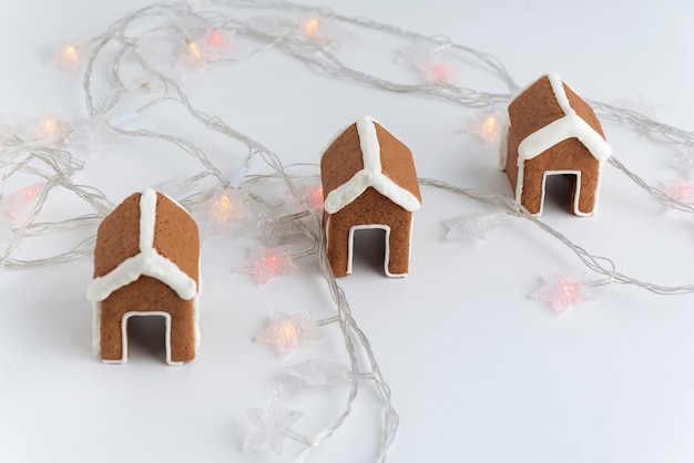Three gingerbread houses for cup on white background next to garlands. Christmas baked goods.