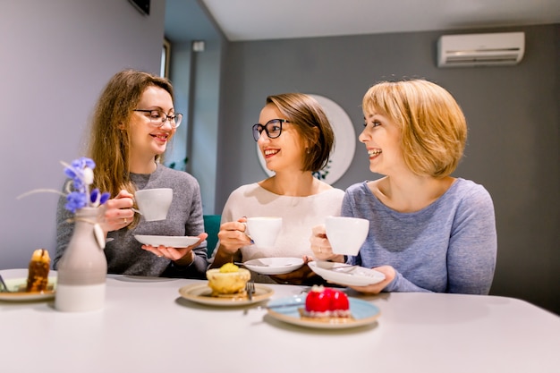 Three girl friends drinking coffee and eating desserts cakes in the cafe indoors