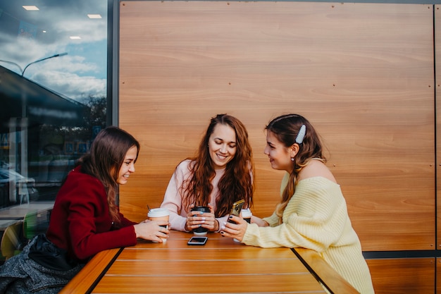 Фото Три подружки сидят в кафе за столом, пьют кофе и разговаривают.