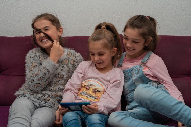 Three girls are sitting on the couch and using a smartphone playing games or watching video