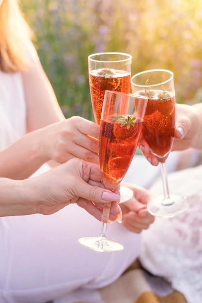 Photo three girls clink glasses with sparkling wine and strawberries inside at a picnic