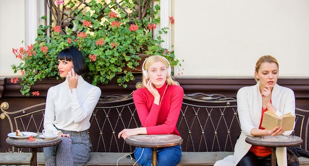 Three girls do different things different ways to relax girls in cafe social diversity listening music reading book speaking on phone frienship free time spending relax business meeting