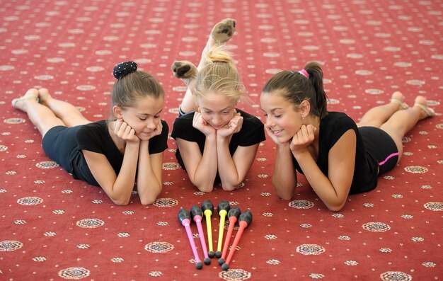 Three girls on the floor looking at Indian clubs