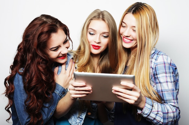 Three girls friends taking selfie with digital tablet, studio shot over gray background