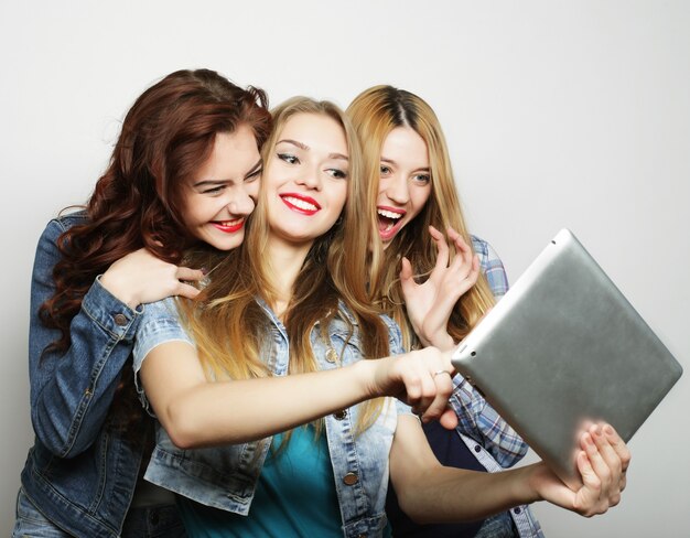 Three girls friends taking selfie with digital tablet, studio shot over gray background