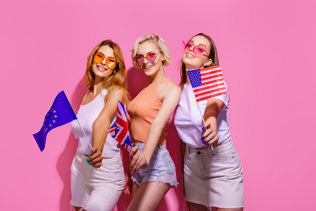 Three girls in summer clothes glasses holding flags of the european union united states and britain ...