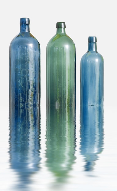 水の効果のある白い表面に3本のガラス瓶コピースペースの背景に反射して配置された古いカラフルなヴィンテージワインボトル未使用の容器の降順の側面図