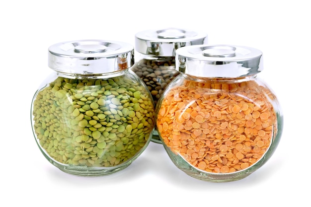 Three glass jars with green, red, brown lentils isolated  