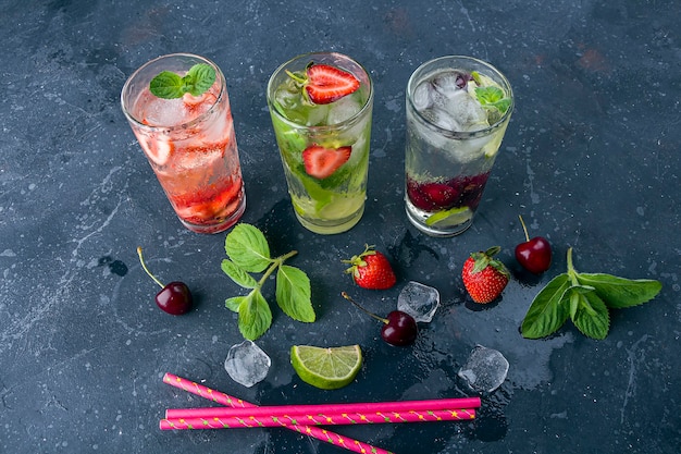 Three glass of refreshing cool detox drink with strawberry, lime, cherry and mint on dark background.