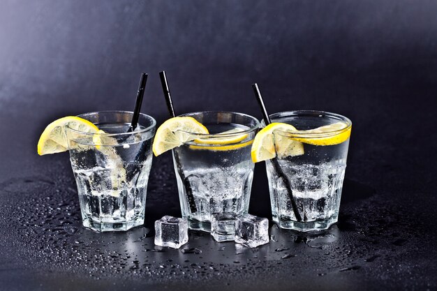 Three glasses of fresh cold carbonated water with ice cubes and lemon slices 