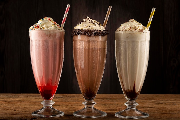 Tre bicchieri di milkshake con gusti assortiti. frappè al cioccolato, vaniglia e fragola.