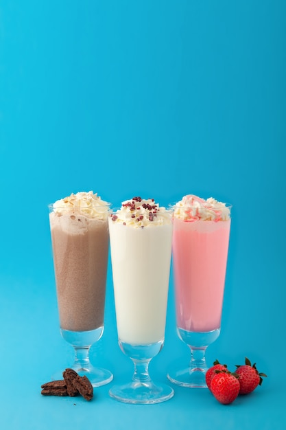 Three glasses milkshakes, vanilla strawberry chocolate on blue background