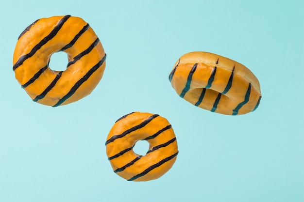 Three glazed orange doughnuts flying on a blue surface