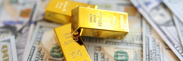 Three gold bullions on background of us dollars banknotes close up financial success exchange