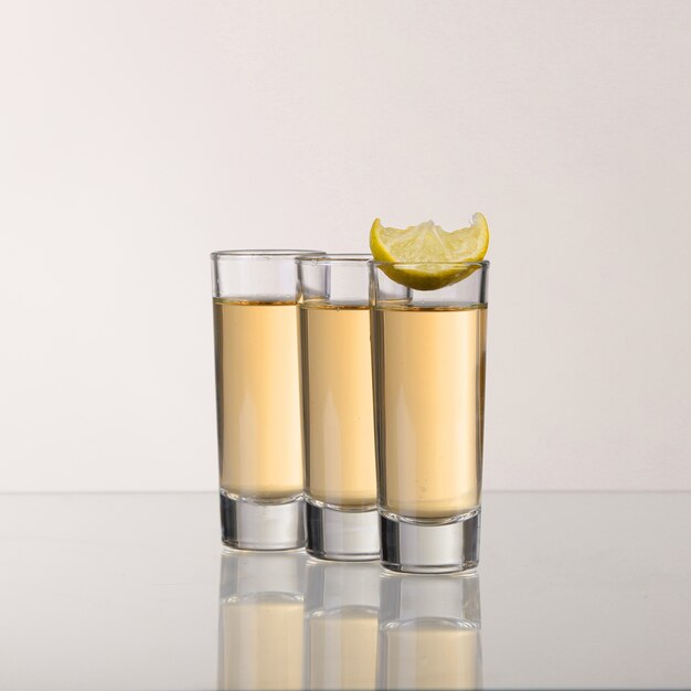 Three gold tequila shots with lime on grey background