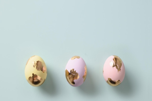 Three golden pastel eggs on blue background Flat lay Happy Easter greeting card with copy space Top view