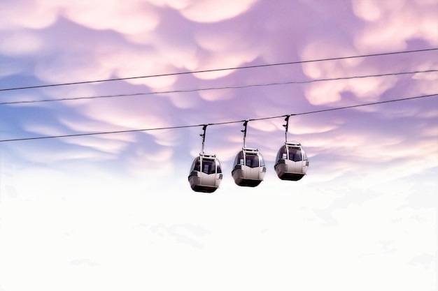 Three gondolas are suspended in the sky with a purple and pink sky in the background