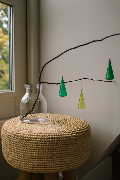 Three green glass christmas baubles on a wood branch in a vase on a  light background and a window. DIY New year and Christmas creative room decor idea. Minimal scandinavian ornament.