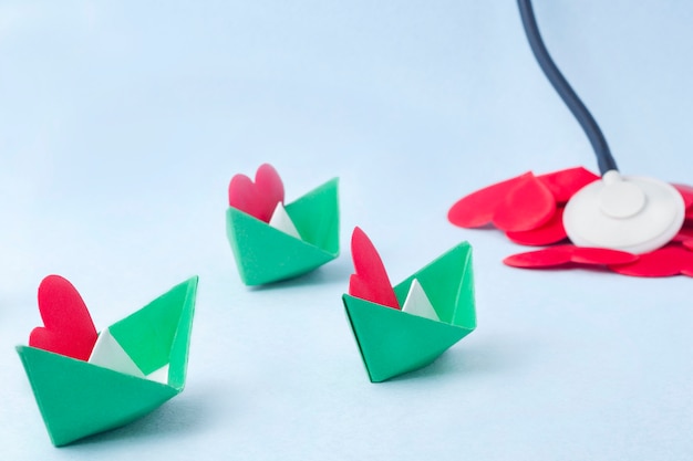 Three green paper boats carrying red hearts.