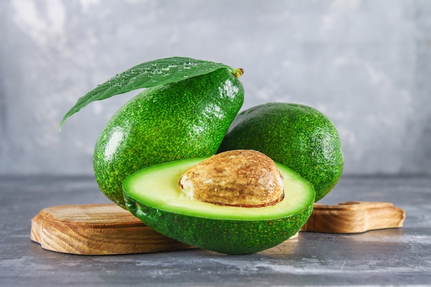 Three green raw ripe avocado fruits and a cut half with a bone with leaves