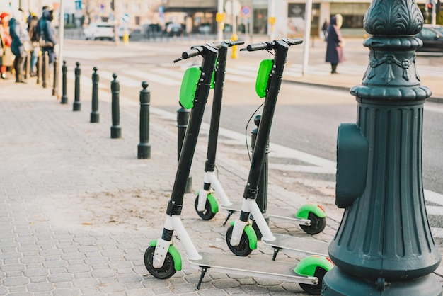 Three green rental electric scooter standing on a sidewalk city\
transport pathway outdoor electric urban transportation