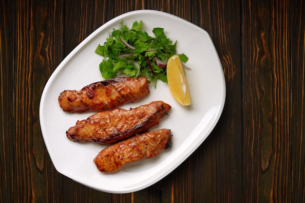 Three grilled pieces of salmon fillet, trout, with herbs and lemon, on a white plate, on a wooden table