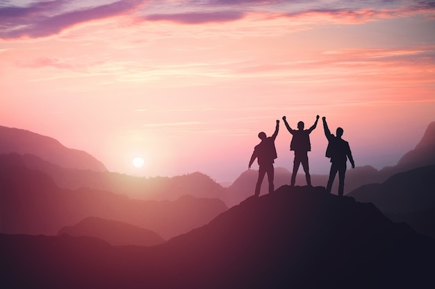 Three guys celebrating victory on top of a mountain at sunset