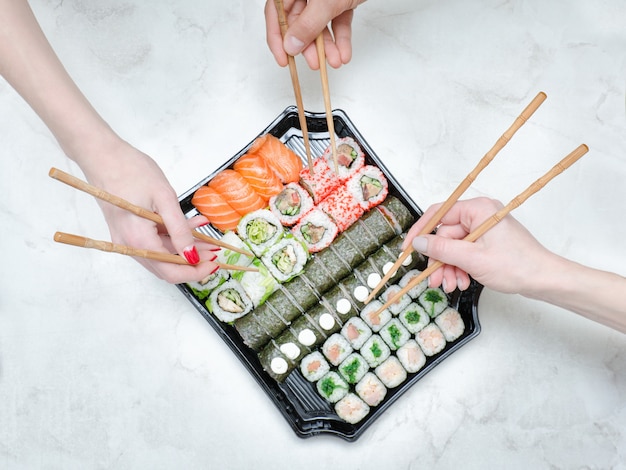 Three hands with chopsticks and sushi set. Top view