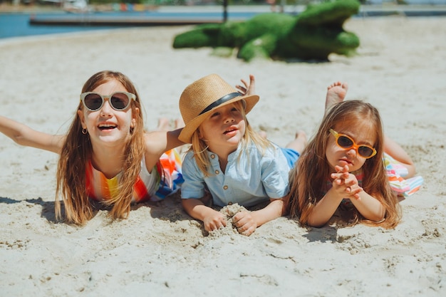 Tre bambini felici giacciono sulla sabbia sulla spiaggiaun bambino con sindrome di down con gli amici si diverte sulla spiaggia