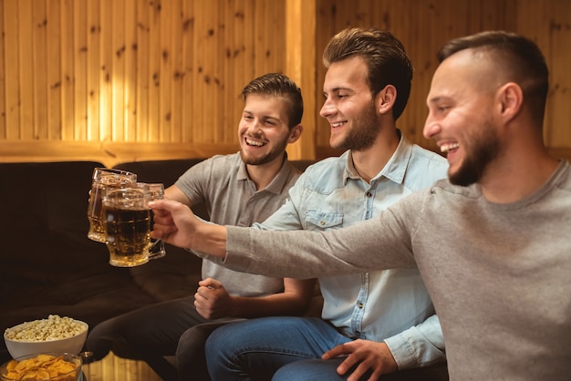 The three happy friends clink glasses with a beer