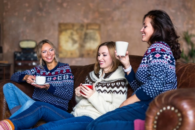 Three happy friends drinking coffee while relaxing on the sofa