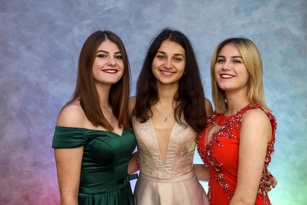 Three happy girls in elegant dresses posing on abstract background. Celebration concept