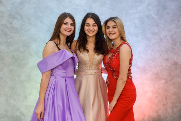 Three happy girls in elegant dresses posing on abstract background. Celebration concept