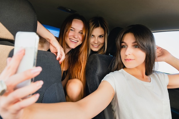 Tre viaggiatrici sorridenti felici che posano insieme per una foto mobile su un meraviglioso viaggio su strada, selfie con gli amici, ricordi felici.