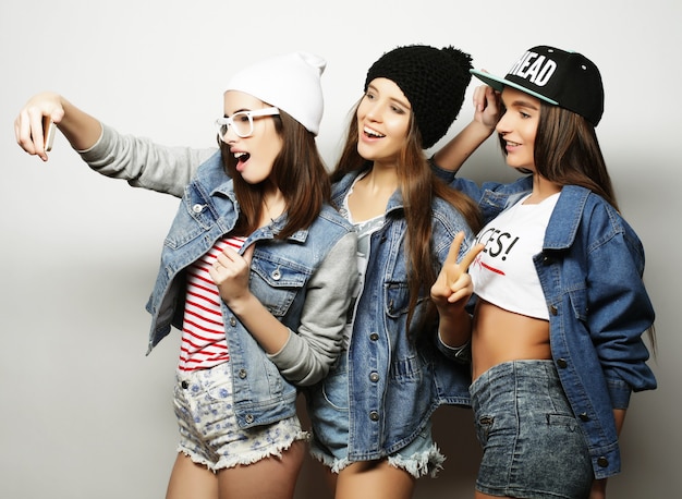 Three happy teenage hipster  girls with smartphone taking selfie