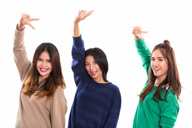 一緒に腕を上げてピースサインをしながら笑っている3人の幸せな若いアジアの女性の友人