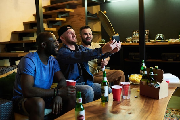 Photo three happy young intercultural buddies making selfie on smartphone