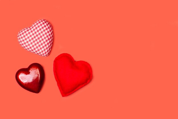 Three hearts made with fabric and plastic on a red background in a top view