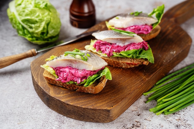 Three herring sandwiches with beet and green salad leaves on wooden board Close up Omega 3 fats source Brain food concept Home cooking