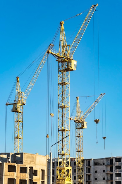 Three high construction tower cranes against the blue sky Construction of a multistorey building