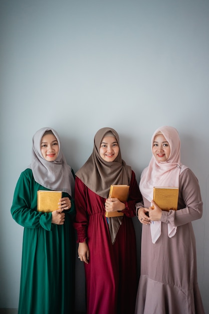 Three hijab women smilling hold the holy book of Al-Quran