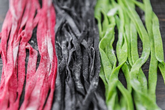 Three home-made pasta on a dark wooden background. black pasta with cuttlefish ink, green pasta with spinach and pink paste