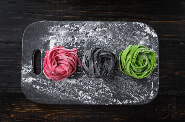 Три самодельной пасты на темном деревянном столе. черная паста с чернилами каракатицы, зеленая паста со шпинатом и розовой пастой