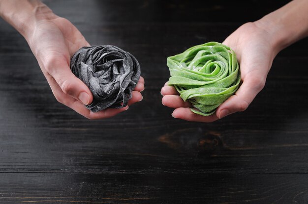 Three home-made pasta on a dark wooden table. black pasta with cuttlefish ink, green pasta with spinach and pink paste