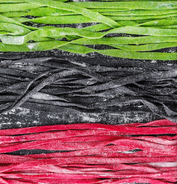 Three home-made pasta on a dark wooden table. black pasta with cuttlefish ink, green pasta with spinach and pink paste