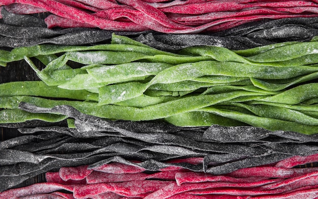 Three home-made pasta on a dark wooden table. black pasta with cuttlefish ink, green pasta with spinach and pink paste