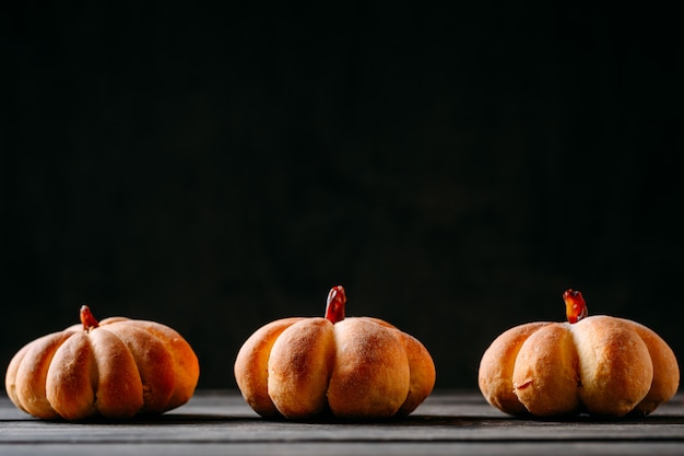 Three homemade cakes in the shape of a pumpkin on dark with copy space